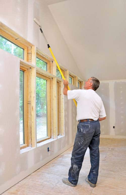 Man priming a wall using a roller attached to an extension pole.